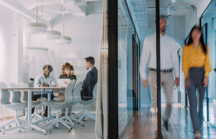 Two People Walking By An Occupied Meeting Room