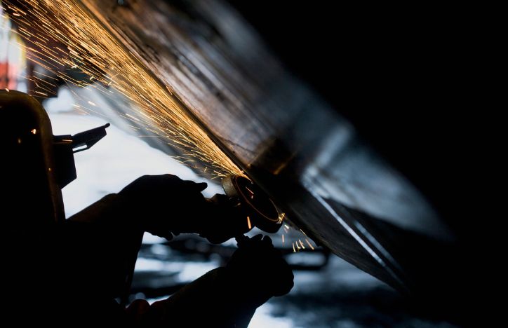 Welder Working With Grinder On Side Of A Boat Hull