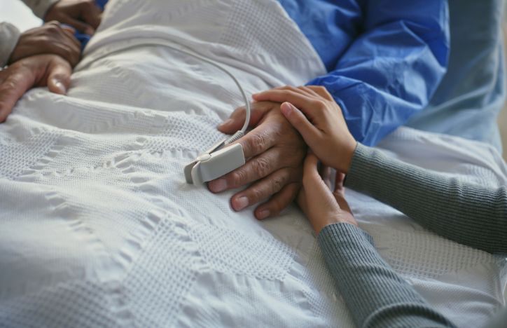 Elderly Man Holding Hands In Hospital Bed